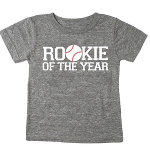 May include: Gray heather short-sleeved t-shirt with white text that reads "Rookie of the Year" and a red and white baseball graphic.