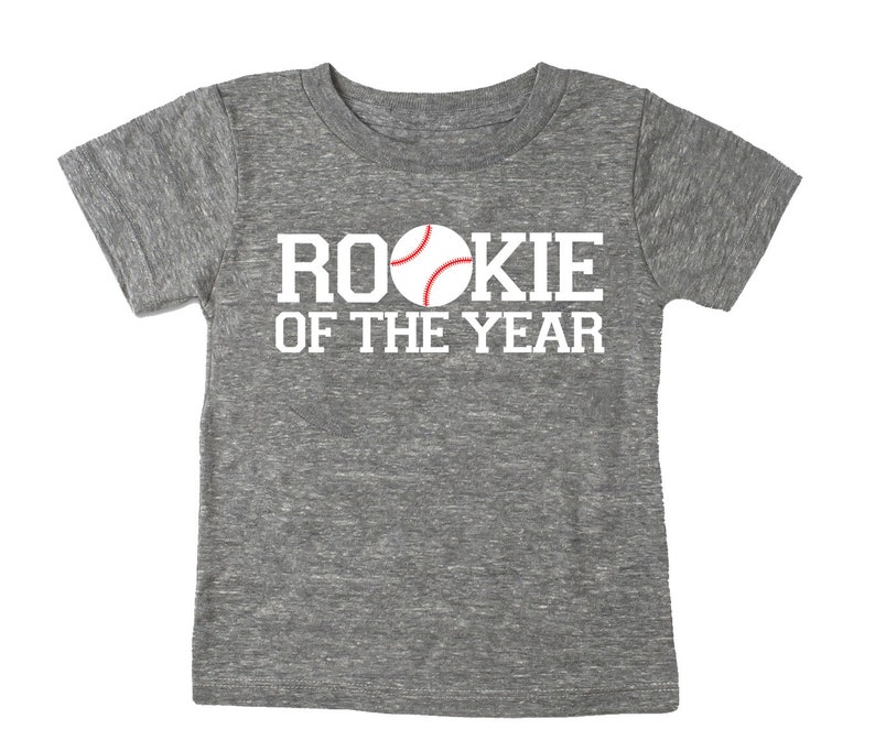 May include: Gray heather short-sleeved t-shirt with white text that reads "Rookie of the Year" and a red and white baseball graphic.