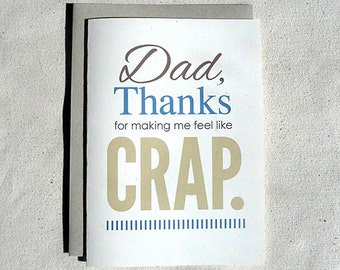 May include: A white card with a brown envelope. The card has the text "Dad, Thanks for making me feel like CRAP." in brown, blue, and yellow lettering. There are blue lines at the bottom of the card.