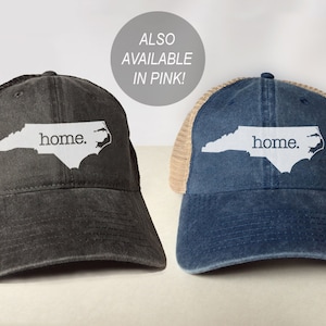 May include: Two trucker hats with a mesh back. The hats are black and blue with a white outline of the state of North Carolina and the word "home." printed on the front.