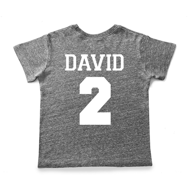Pu&ograve; includere: Una maglietta grigia melange con il nome "DAVID" e il numero "2" stampati in bianco sul retro.