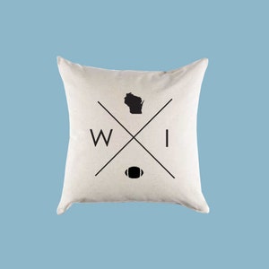 Puede incluir: Una almohada blanca con un dise&ntilde;o en blanco y negro que presenta el estado de Wisconsin, un bal&oacute;n de f&uacute;tbol y las letras "WI".