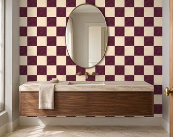 Puede incluir: Un mueble de baño con un gabinete flotante de madera oscura, encimera de piedra clara, lavabo rectangular y grifo dorado. Sobre el mueble hay un espejo ovalado montado en una pared con un patrón de cuadros en tonos ciruela y crema.