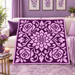 May include: A square throw blanket featuring a dark purple background with a light pink pixelated floral pattern. The design displays a large central flower surrounded by four corner roses and symmetrical scrolling leaf motifs throughout.