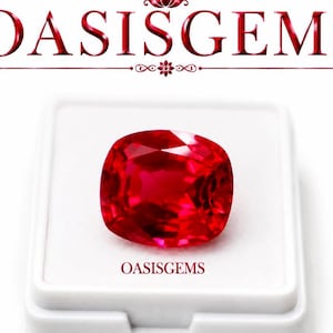 Puede incluir: Una gema roja de corte cojín, vibrante y brillante, presentada en una caja cuadrada blanca. El texto OASISGEMS está impreso en rojo en la parte superior de la imagen y también aparece en una fuente roja más pequeña sobre el inserto blanco.