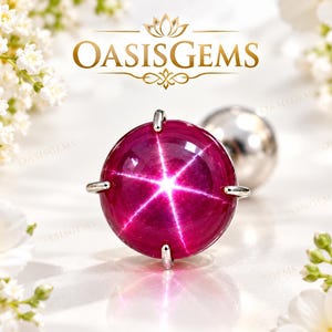 Può includere: Una gemma di rubino stellato rotonda, color magenta intenso, montata su una montatura a griffe in metallo color argento. La pietra tagliata a cabochon mostra un distinto effetto a stella a sei raggi sulla superficie. Il testo OASISGEMS è visibile.