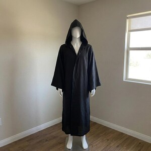 May include: A floor-length black hooded robe with long, wide sleeves and an open front design. The garment features a deep, pointed hood and a loose, flowing silhouette that extends down to the ankles, crafted from a solid black fabric.