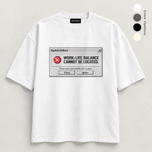 Könnte beinhalten: Ein weißes kurzärmeliges T-Shirt mit einem Grafikdruck eines Computer-Fehlerfensters. Der Text lautet System Failure, WORK-LIFE BALANCE CANNOT BE LOCATED, Please check your priorities and try again, Retry und Ignore. Ein Markenetikett zeigt die Aufschrift CtrlCulture.