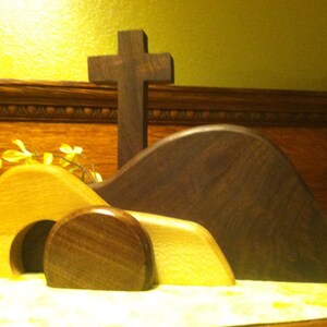 May include: A wooden Easter tomb set with a cross, a yellow flower arrangement, and a brown wooden background.
