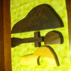 May include: Three wooden shapes, one brown and two light brown, are arranged on a green fabric background. The shapes are abstract and organic in form.