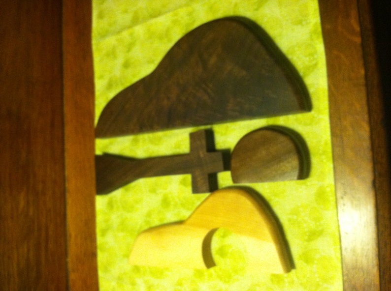 May include: Three wooden shapes, one brown and two light brown, are arranged on a green fabric background. The shapes are abstract and organic in form.