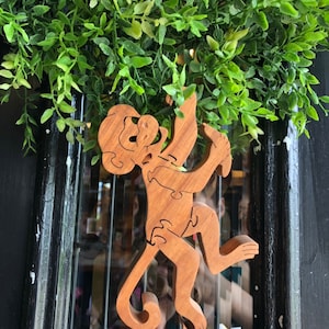May include: A wooden monkey puzzle toy hanging on a black door with green foliage behind it.