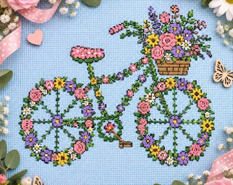 Può includere: Un motivo a punto croce su tessuto azzurro che raffigura un telaio di bicicletta decorato con fiori colorati. Un cestino pieno di fiori rosa, gialli e viola è posizionato sul manubrio. Anche le ruote sono ornate con motivi floreali.