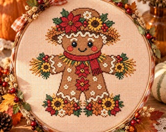 Può includere: Un ricamo a punto croce in un telaio di legno raffigurante un omino di pan di zenzero decorato con stelle di Natale rosse, girasoli gialli e una sciarpa rossa. Il telaio è ornato con foglie autunnali artificiali, bacche e un nastro a quadri.
