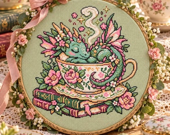 Può includere: Un ricamo a punto croce in un telaio di legno raffigurante un drago verde che dorme in una tazza da tè floreale appoggiata su dei libri. Il disegno include rose rosa, vapore che sale dalla tazza e un nastro rosa legato al telaio.