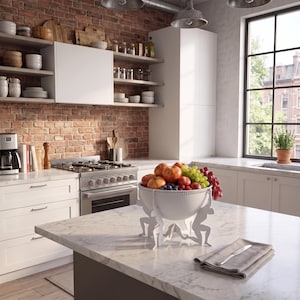 May include: A white decorative fruit bowl featuring a base supported by four stylized human figures in a kneeling position, filled with a variety of fresh apples, grapes, and berries, resting on a white marble kitchen countertop surface.