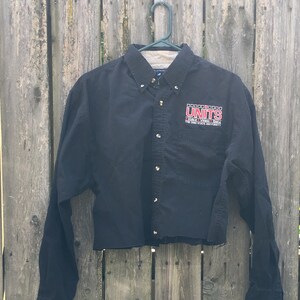 May include: A black long-sleeved button-down shirt with a cropped hem. The shirt has the text "The University of Texas at Austin" and "UNITS" embroidered on the front.