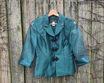 Puede incluir: Una chaqueta de color verde azulado con botones negros y una etiqueta que dice "Amici".