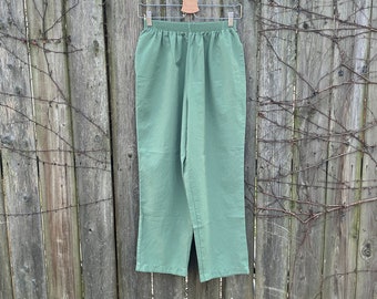 May include: Light green pants hanging on a wooden fence. The pants have an elastic waistband and a straight leg design. The fabric appears to be a lightweight material, suitable for warmer weather. The pants are displayed outdoors in natural light.
