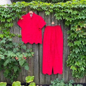 May include: A red two-piece outfit with a short-sleeved button-up top and matching pants. The top has a scalloped hem and the pants have a scalloped hem at the bottom.