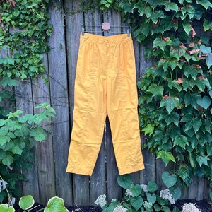 May include: A pair of yellow high-waisted pants with a zipper and button closure. The pants are made of a lightweight fabric and have a relaxed fit.