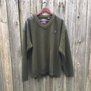May include: A green knitted sweater with a v-neck and a small patch on the front that says "Z.I.A."