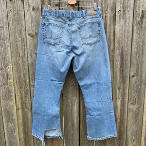 May include: A pair of light blue denim jeans with a distressed hem. The jeans have a straight leg and are hanging on a wooden hanger.