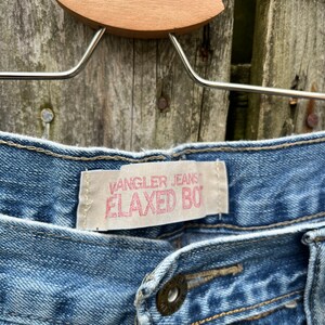 May include: A pair of blue denim jeans with a Wrangler Jeans Relaxed Boy label. The jeans have a button fly and a single button on the waistband.