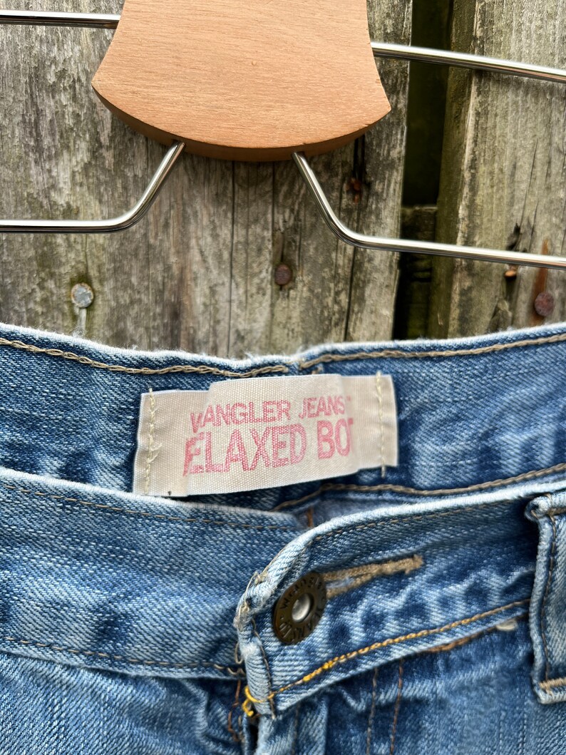 May include: A pair of blue denim jeans with a Wrangler Jeans Relaxed Boy label. The jeans have a button fly and a single button on the waistband.