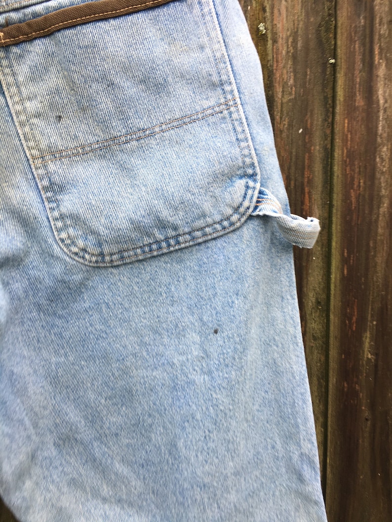 May include: A pair of light blue denim jeans with a brown leather belt loop and a large back pocket.