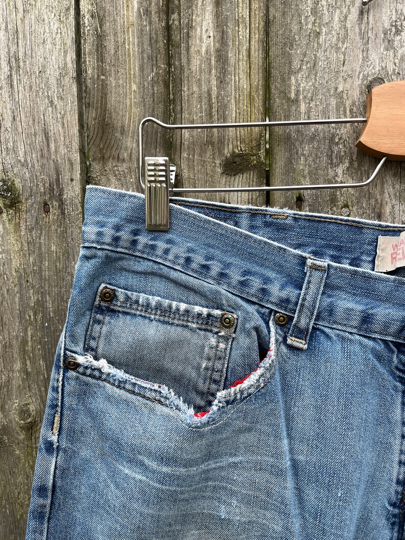 May include: A pair of blue denim jeans with a red and white plaid lining peeking out from a ripped pocket.