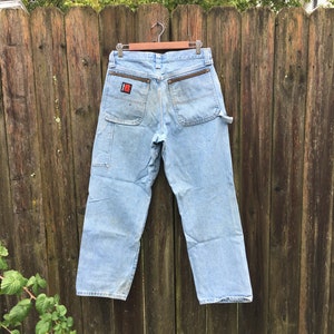 May include: Light blue denim carpenter jeans with a brown leather patch on the back pocket. The patch has a red and white logo.