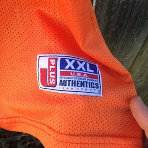K&ouml;nnte beinhalten: Orangefarbenes Mesh-Trikot mit einem wei&szlig;en und blauen Etikett mit der Aufschrift "U.S.A. XXL Plus Offiziell lizenziertes Produkt Authentics Team Sports".