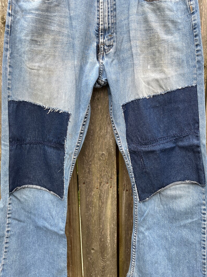 May include: A pair of blue denim jeans with two large dark blue denim patches sewn on the knees.