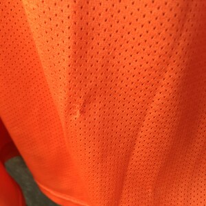 K&ouml;nnte beinhalten: Nahaufnahme eines leuchtend orangenen Stoffes mit einem kleinen Loch. Der Stoff hat ein Netz-Muster.