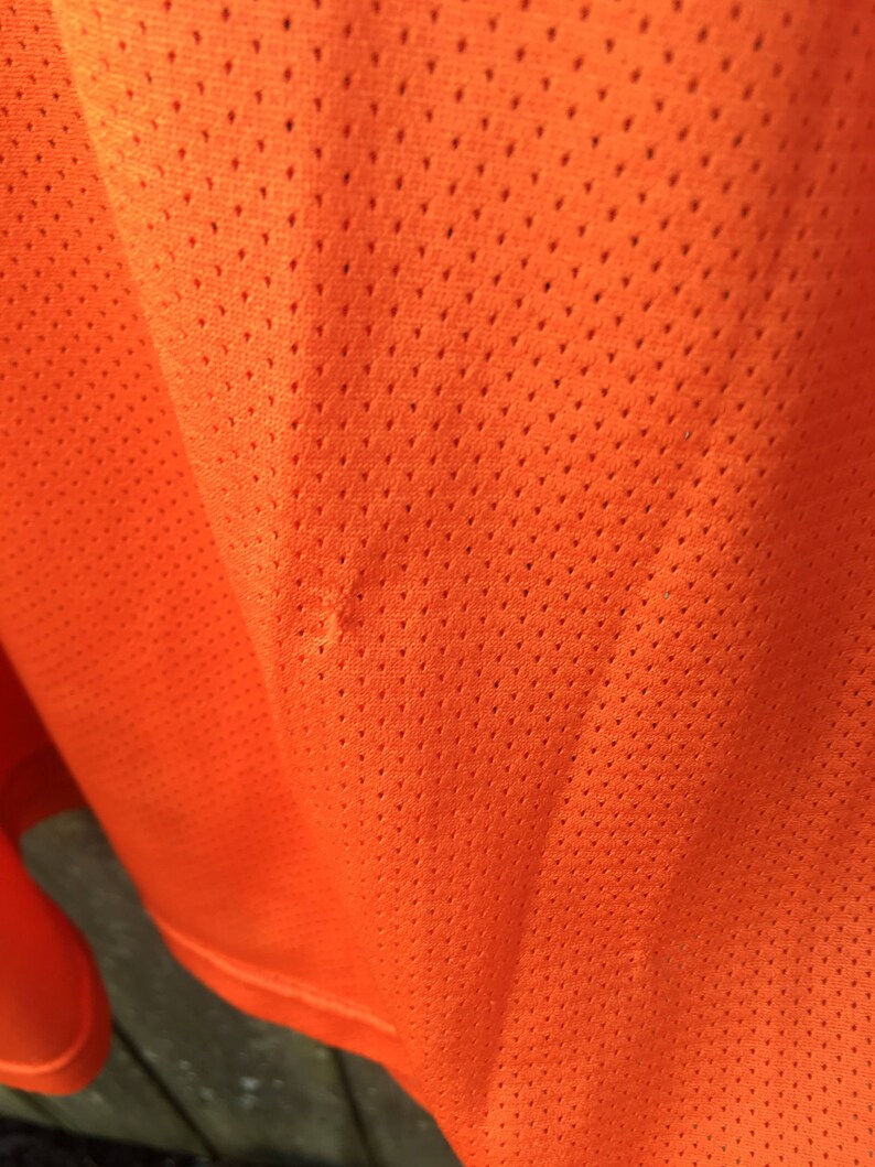 K&ouml;nnte beinhalten: Nahaufnahme eines leuchtend orangenen Stoffes mit einem kleinen Loch. Der Stoff hat ein Netz-Muster.