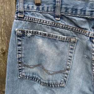 May include: A pair of light blue denim jeans with a back pocket. The pocket has a faded white mark and a brown stitching detail.