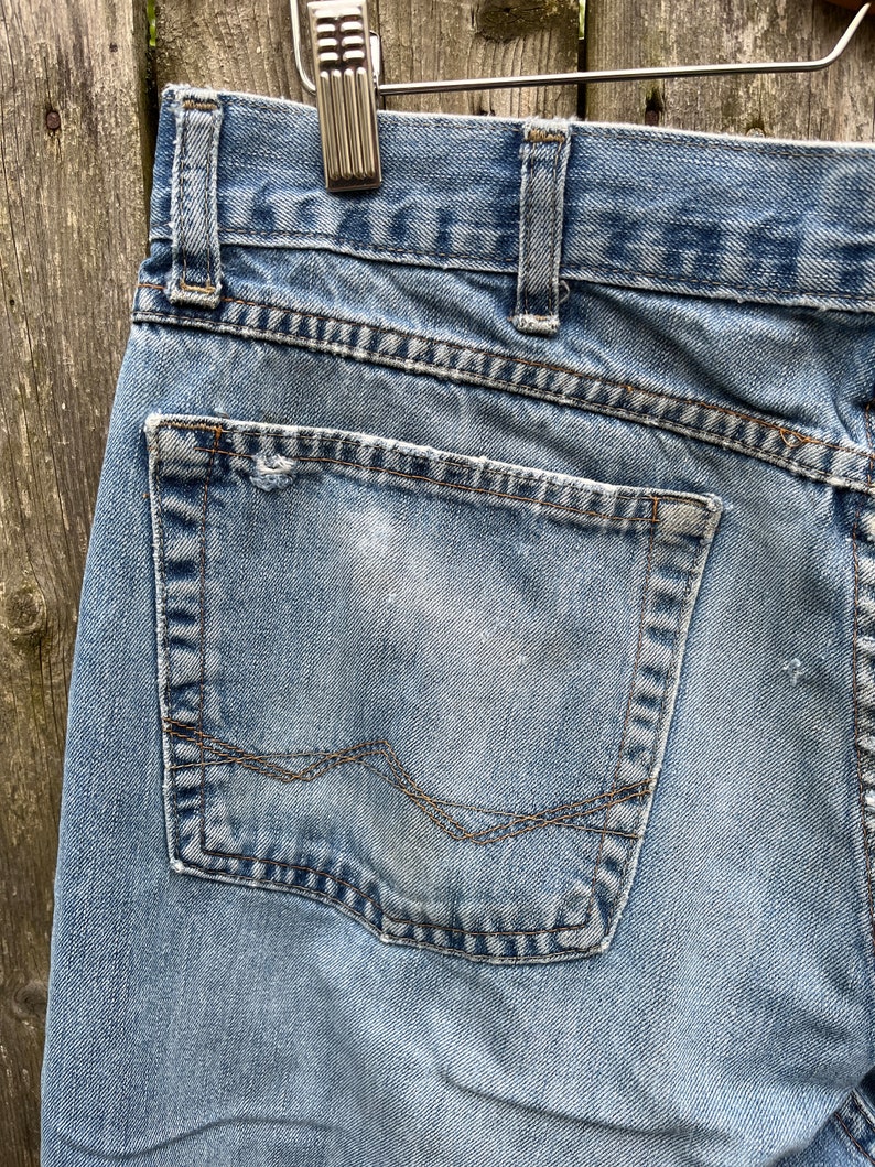 May include: A pair of light blue denim jeans with a back pocket. The pocket has a faded white mark and a brown stitching detail.