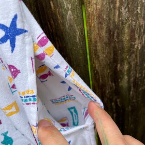 May include: White sleeveless shirt with a colourful fish and starfish pattern. The shirt has a pocket on the left side.