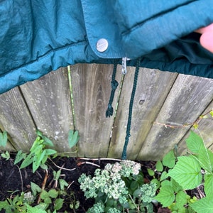 May include: A dark green hooded jacket with a zipper and a drawstring. The jacket has a silver button and a small logo on the front.