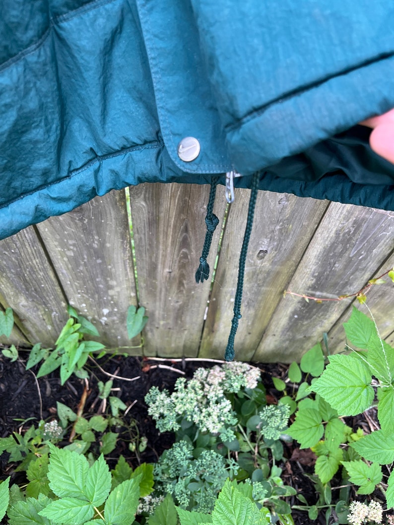 May include: A dark green hooded jacket with a zipper and a drawstring. The jacket has a silver button and a small logo on the front.