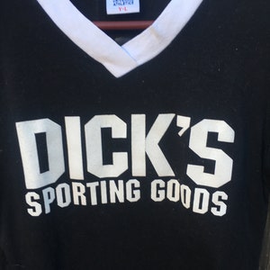 May include: Black v-neck t-shirt with white trim and the text "DICK'S SPORTING GOODS" in white block letters. The shirt has a tag that reads "UNIVERSAL ATHLETICS Y-L".