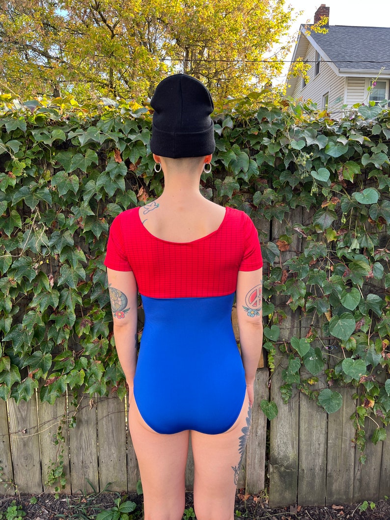 Pu&ograve; includere: Un costume da bagno intero rosso e blu con maniche corte. Il costume da bagno ha una parte superiore rossa con un motivo a righe orizzontali e una parte inferiore blu tinta unita.