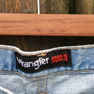 May include: Light blue denim jeans with a black Wrangler label and a red and white Riggs Workwear label.