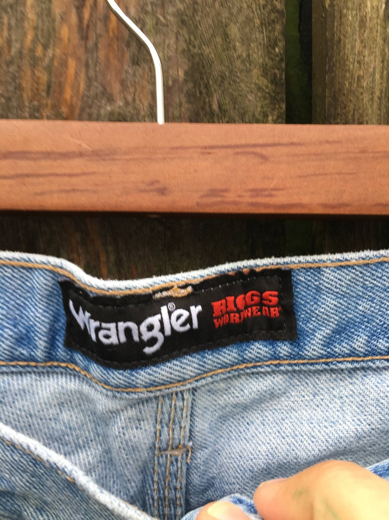 May include: Light blue denim jeans with a black Wrangler label and a red and white Riggs Workwear label.