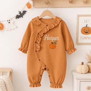 May include: A long-sleeved, ribbed, burnt orange romper featuring a ruffled trim along the diagonal front closure. The garment is embroidered with the name Harper in white script and a small orange pumpkin graphic on the chest area.