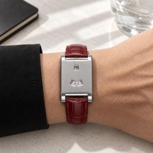 Könnte beinhalten: Eine rechteckige Armbanduhr mit einem gebürsteten silberfarbenen Metallgehäuse und einem dunkelroten Lederarmband mit Alligatorprägung. Das Zifferblatt zeigt ein kleines Datumsfenster mit der Zahl 3 und eine bogenförmige Minutenanzeige.