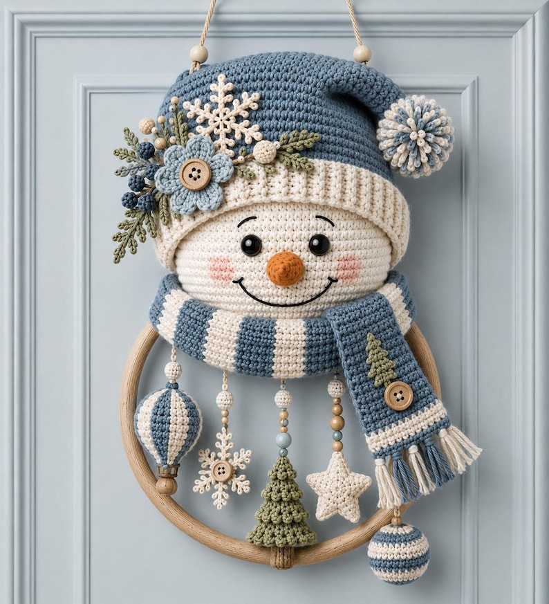 May include: A crocheted snowman wall hanging featuring a blue and cream striped hat with a pom-pom, a matching scarf, and a round wooden frame. The snowman is decorated with a crocheted flower, snowflake, and dangling ornaments including a star, tree, and spheres.