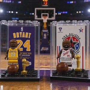 Peut inclure: Deux vitrines en plastique transparent contenant des figurines Kobe Bryant. La vitrine de gauche présente un maillot jaune des Lakers avec le numéro 24, un ballon de basket et un trophée. Celle de droite montre un maillot All-Star avec le numéro 24.