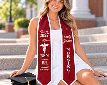 May include: A maroon graduation stole with white trim featuring the text Class of 2027, a heart with an EKG line, a caduceus symbol, BSN, RN, University of Georgia, Emily Johnson, and NURSING. A black graduation cap with a gold tassel is included.